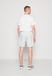 Camiseta branca e calções cinza claro feitos de tecido macio, com uma cintura elástica. A visão traseira mostra mangas curtas e um design minimalista.