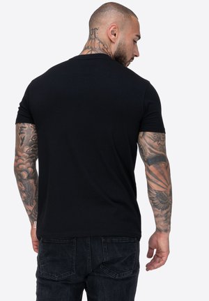 Camiseta corta de manga negra, diseño ajustado, tela de algodón, cuello redondo, espalda lisa, el usuario tiene tatuajes visibles en los brazos.