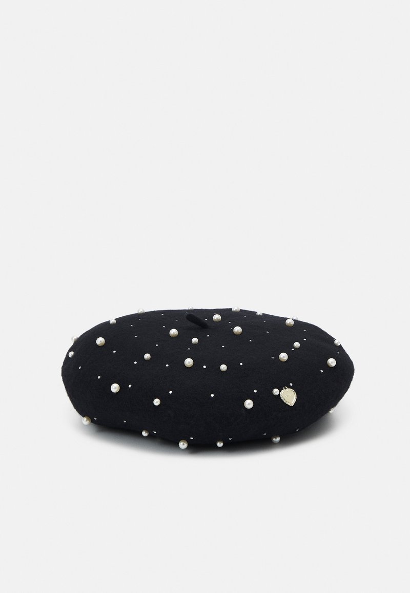 Béret en laine noire orné de perles blanches éparses et d'un petit charme métallique en forme de cœur sur un fond uni.