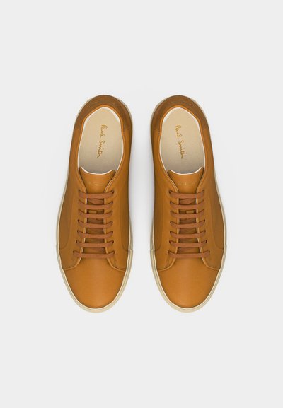 Ζευγάρι καφέ δερμάτινα sneakers με κορδόνια και λευκές σόλες, σε λευκό φόντο, απεικονιζόμενα από πάνω.