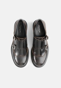 Zwarte lederen schoenen met geperforeerde details, tan accenten en twee zilveren gespen. Rondneus en stevige rubberen zool.