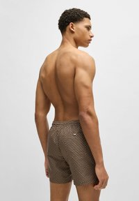 Brown patterned swim shorts with an elastic waistband and a small logo accent. The fabric appears textured and lightweight.