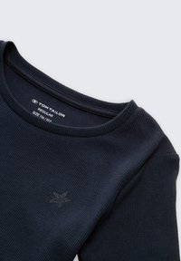 Donkerblauw geribbeld t-shirt met lange mouwen, ronde hals en een klein geborduurd sterrenlogo op de borst. Maatlabel geeft 116-122 aan.