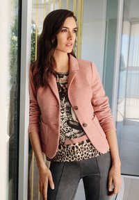 Vaaleanpunainen villatakki, jossa on kaksi nappia, kerrostettuna eläinkuosilla varustetun paidan päälle, yhdistettynä tummanharmaisiin legginsseihin. Sileä rakenne, tiukka muotoilu.