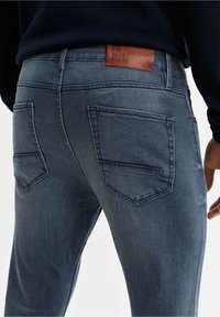 Jeans de mezclilla índigo con un parche de cuero etiquetado "BLUE RIDGE", bolsillos traseros cerrados y un corte slim con un leve desgaste.