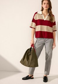 Červeno-beige pruhované polo tričko s krátkým rukávem, šedé džíny, černé lakované mokasíny a zelený batoh se stahovací šňůrkou a červenou rukojetí.