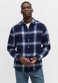 Blau-schwarz karierte Flanellhemd mit weißen horizontalen Streifen, Knopfverschluss und Kragen. Über einem weißen T-Shirt getragen, kombiniert mit Jeans.