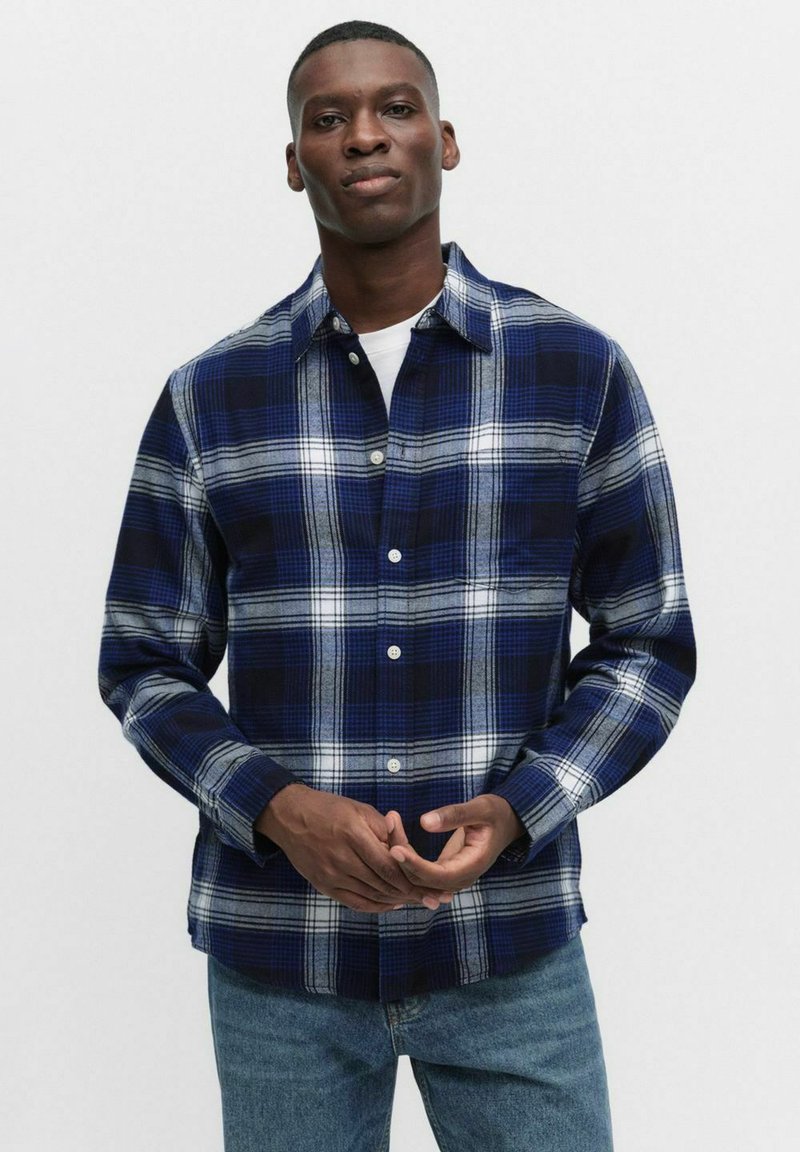 Niebieska i czarna flannelowa koszula w kratę z białymi poziomymi paskami, zapinana na guziki, z kołnierzykiem. Noszona na biały t-shirt, zestawiona z dżinsami.