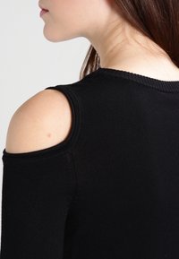 Czarny top z odkrytymi ramionami, z prążkowanym dekoltem i krawędziami rękawów. Charakteryzuje się dopasowanym krojem i gładką fakturą.