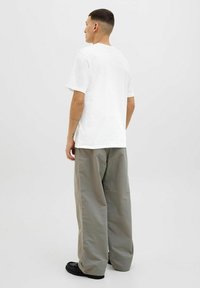 Hvid bomulds T-shirt med rund hals, båret med løse, lysegrå bukser og sorte sko, set fra ryggen.
