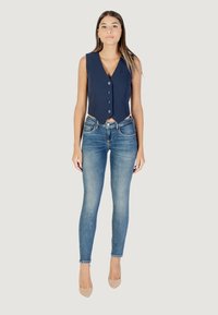 Gilet sans manches navy avec un col cranté et six boutons, associé à un jean skinny bleu clair et des talons hauts nude.