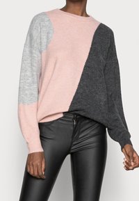 Pull en maille avec design colorblock en rose, gris clair et gris foncé. Caractérisé par un col rond et une coupe décontractée. Associé à un pantalon en cuir noir.