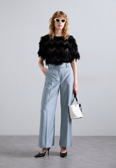 Must mustriga konksu mustade kiilude, helesinised kõrge vöökohaga laiad püksid, mustad teravatipulised kontsad ja väike must-valge käekott.