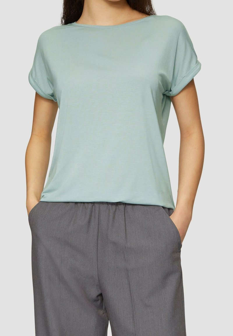 Chemise légère bleu clair à manches courtes avec un col rond et des manches retroussées, associée à un pantalon gris à taille élastique avec des poches latérales.