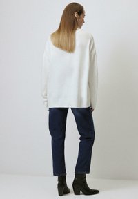 Oversized white sweater with a ribbed hem, paired with dark blue straight-leg jeans and black ankle boots. Smooth texture, relaxed fit.