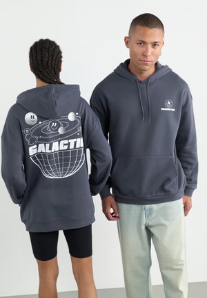 Sivi pull hoodie s prednjim džepom. Grafički dizajn na leđima prikazuje planete i tekst "GALAKTIČKI" u bijeloj boji. Mekana, teksturirana tkanina.
