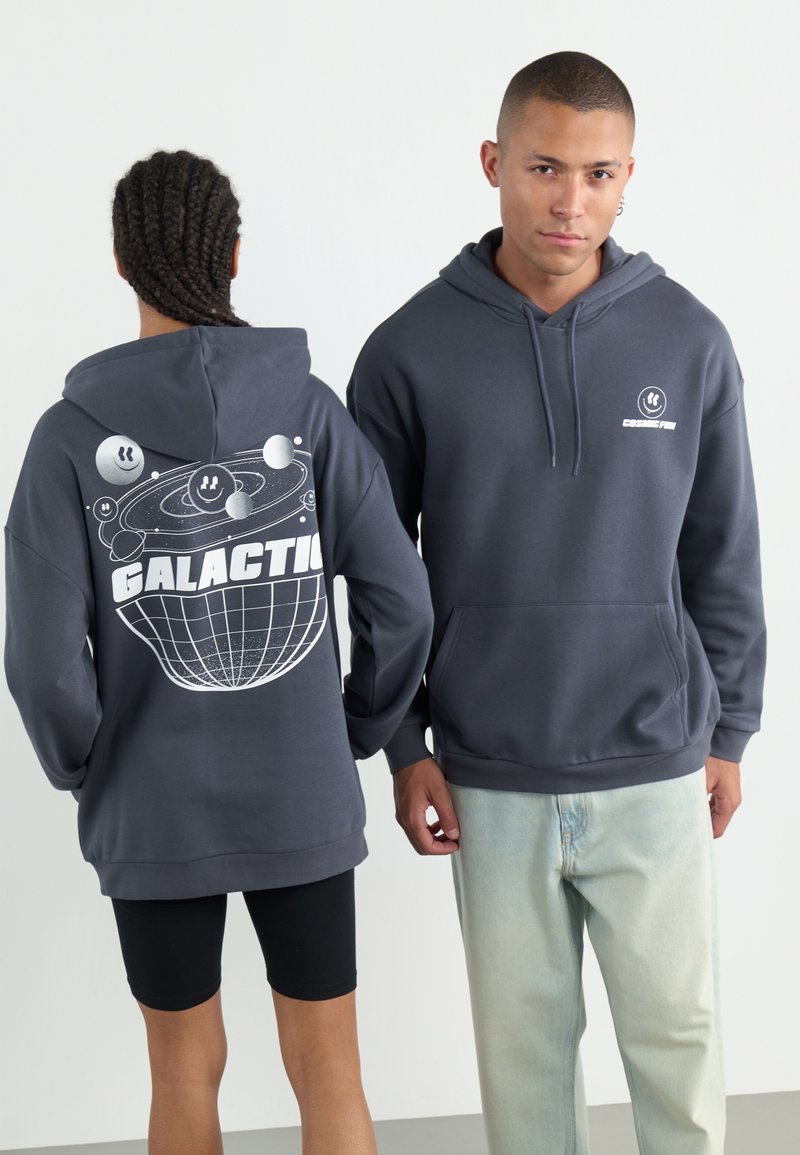Felpa grigia con cappuccio e tasca frontale. Il design grafico sul retro presenta pianeti e la scritta "GALACTIC" in bianco. Tessuto morbido e texture.