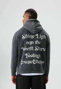 Sweat-shirt à capuche gris à coupe ample, présentant un texte blanc au dos avec des phrases motivantes. Tissu doux, style décontracté.