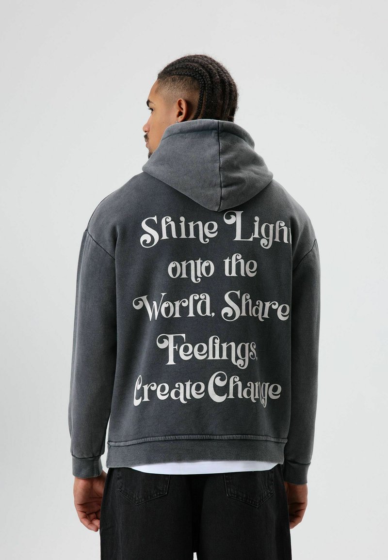 Sweat-shirt à capuche gris à coupe ample, présentant un texte blanc au dos avec des phrases motivantes. Tissu doux, style décontracté.
