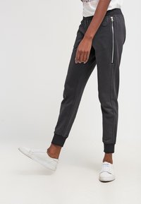 Grau Jogginghosen aus weichem Material, mit einer seitlichen Reißverschlusstasche, gerippten Bündchen und einem schlanken Schnitt. Kombiniert mit weißen Sneakers.