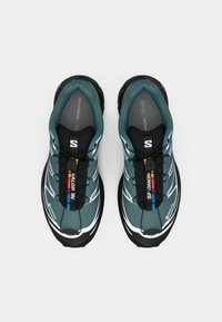 Atletische schoenen, met een turquoise bovenkant en zwarte accenten, witte details en een gestructureerde zwarte zool. Inclusief een GORE-TEX-label en elastische veters.