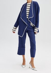 Modrá bunda s bílým lemem a volným střihem, doplněná pruhovaným tričkem s dlouhým rukávem, modrými zkrácenými kalhotami a stříbrnými lodičkami na podpatku.