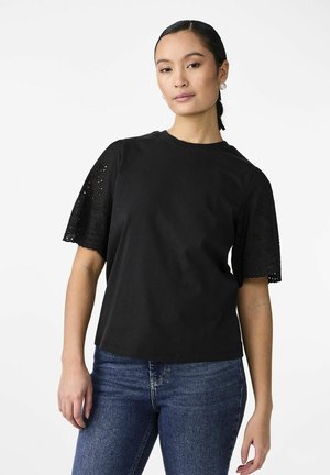 Zwarte t-shirt met korte, intricately gedetailleerde kantmouwen. Ronde halslijn en een relaxte pasvorm, gecombineerd met blauwe spijkerbroeken.