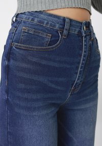 Μπλε τζιν από τζιν υλικό με άνετη εφαρμογή, ορατές ραφές και μια πίσω τσέπη. Το ύφασμα έχει διακριτικό ξεθώριασμα και απαλό υφή.