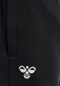 Czarna tkanina z pionowym szwem i białym stylizowanym logo pszczoły w pobliżu dolnego prawego rogu.