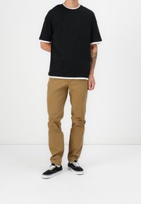 Czarny t-shirt z białymi wykończeniami, khaki spodnie i czarne trampki z białymi podeszwami. Casualowy strój o luźnym kroju i prostym designie.