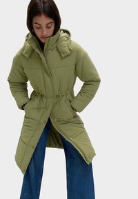 Oliwkowo-zielony pikowany płaszcz z wiązaniem w talii, kieszeniami na suwak i kapturem. Charakteryzuje się teksturowaną powierzchnią i zapięciem na zatrzaski.