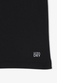 Czarna koszulka sportowa z teksturowanej tkaniny, z białą metką "ULTRA DRY" w dolnym rogu. Krótkie rękawy i klasyczny krój.