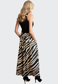 Zwart en beige maxi-jurk met zebra-print, voorzien van een brede tailleband, plooien en zakken. Gestyled met een mouwloos zwart topje en hoge hakken.