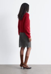 Roter gerippter Pullover mit langen Ärmeln, kombiniert mit einem strukturierten grauen Spitzenrock. Braune gerippte Socken und schwarze Absätze vervollständigen das Outfit.