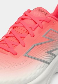 Baskets de course corail vif avec lacets roses, tige en mesh respirante, logo New Balance argenté et semelle blanche rembourrée.