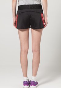 Svarta sportshorts med röda sidostrupror, gjorda av lättmesh-material. Elastisk midja för komfort. Bärs med lila träningsskor.