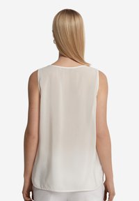 Vitt ärmlöst linne med en slät och lätt textur. Baksidan har en rundad halsringning och en böjd fåll för en avslappnad passform.