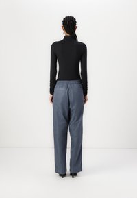 Schwarzes Langarmoberteil mit hohem Kragen, kombiniert mit lockeren, blau-grauen Hosen, die einen elastischen Bund und zwei Gesäßtaschen haben.
