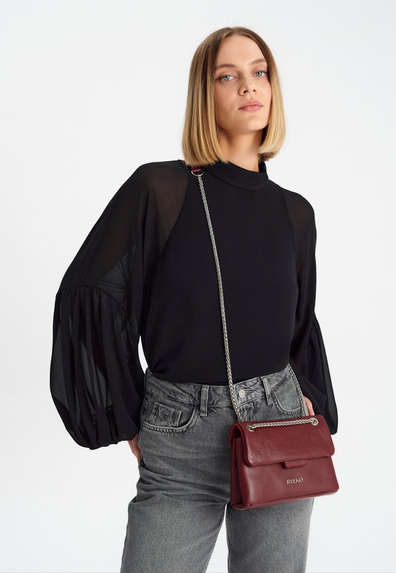 Blusa nera con maniche trasparenti, jeans grigi a vita alta e una piccola borsa in pelle bordeaux con tracolla a catena e chiusura a pattina.