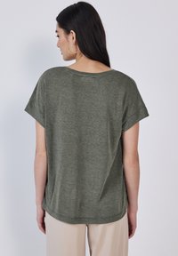 T-shirt verde oliva a maniche corte con vestibilità rilassata, scollo rotondo e texture morbida. Presenta un design semplice con dettagli di cucitura minima.
