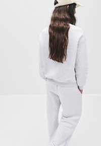 Grijze katoen sweatshirt en bijpassende broek. Zachte textuur, relaxte pasvorm. Achteraanzicht toont lang haar en een lichte pet.