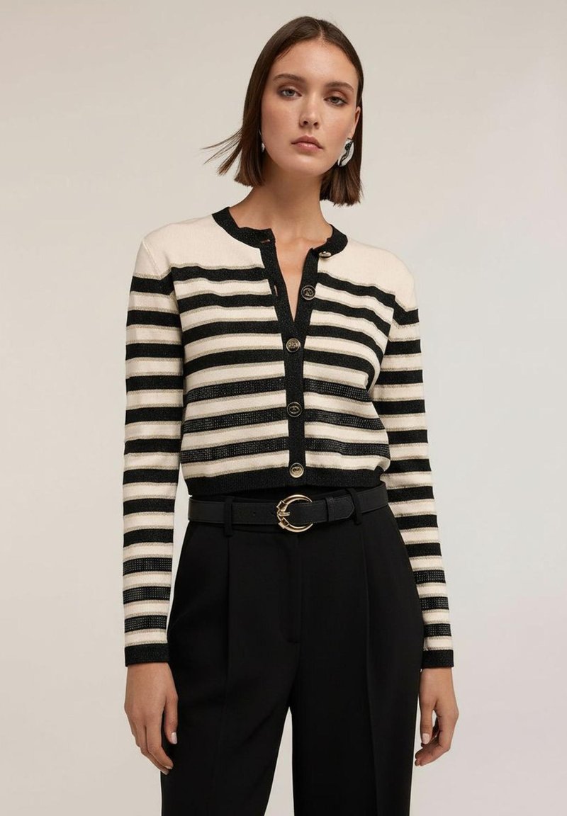 Randig kofta i krämvitt och svart, med knäppning framtill och ribbad textur. Kombinerad med högmidjade svarta byxor och ett bälte.