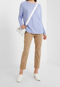 Svetle fialový žebrovaný svetr, béžové slim fit kalhoty, bílé muly a bílá kabelka se zvlněným popruhem a zlatými detaily.