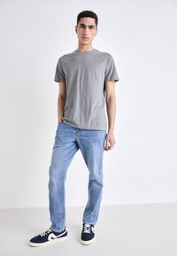 Camiseta gris de manga corta combinada con jeans azul claro y zapatillas marinas con acentos blancos. Atuendo sencillo y casual.