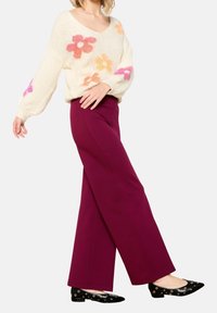 Pletený krémový svetr s barevnými květinovými vzory, doplněný vínovými širokými kalhotami a černými balerínkami se stříbrnými průchodkami.