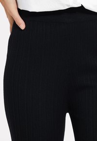 Zwarte geribbelde legging met een soepele elastische tailleband. De stof heeft een rekbare en aansluitende textuur, ideaal voor casual draagcomfort.