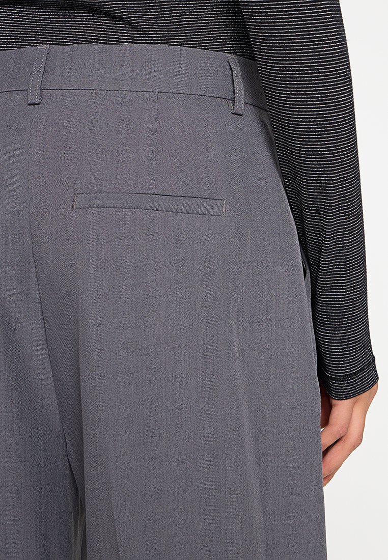 Graue Hosen zeichnen sich durch eine glatte Textur, eine einzelne Gesäßtasche und eine figurschmeichelnde Passform aus. Der Bund hat Gürtelschlaufen für zusätzlichen Stil.