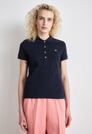 Navy blue polo shirt made of cotton, featuring a collar, short sleeves, and five-button placket. Small logo on the chest is visible.