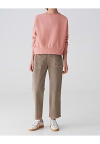 Felpa rosa chiaro con collo rotondo e polsini a coste, abbinata a pantaloni larghi beige. Scarpe bianche con dettagli pastello completano l'outfit.
