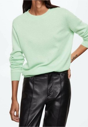 Pull en maille vert clair avec un col rond et des poignets côtelés, associé à un pantalon en cuir noir avec des poches latérales et une finition élégante.